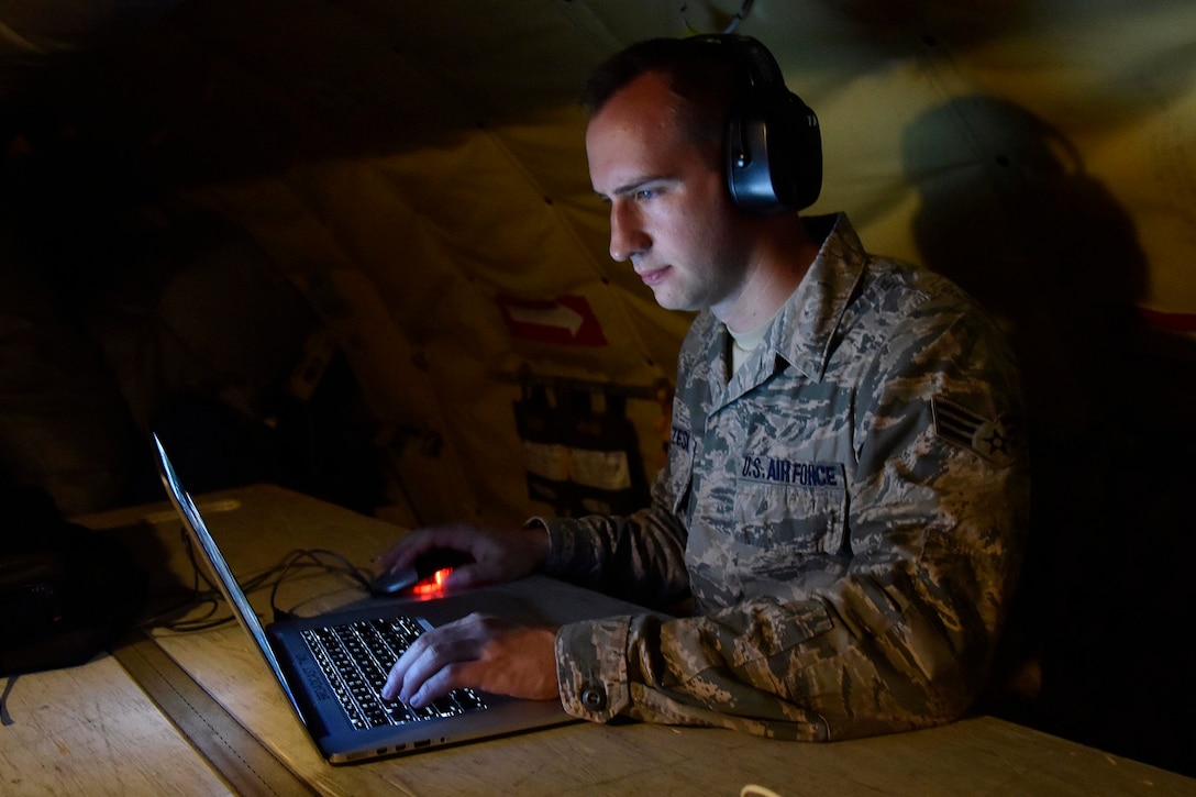 An airman clicks a mouse while looking at a laptop.