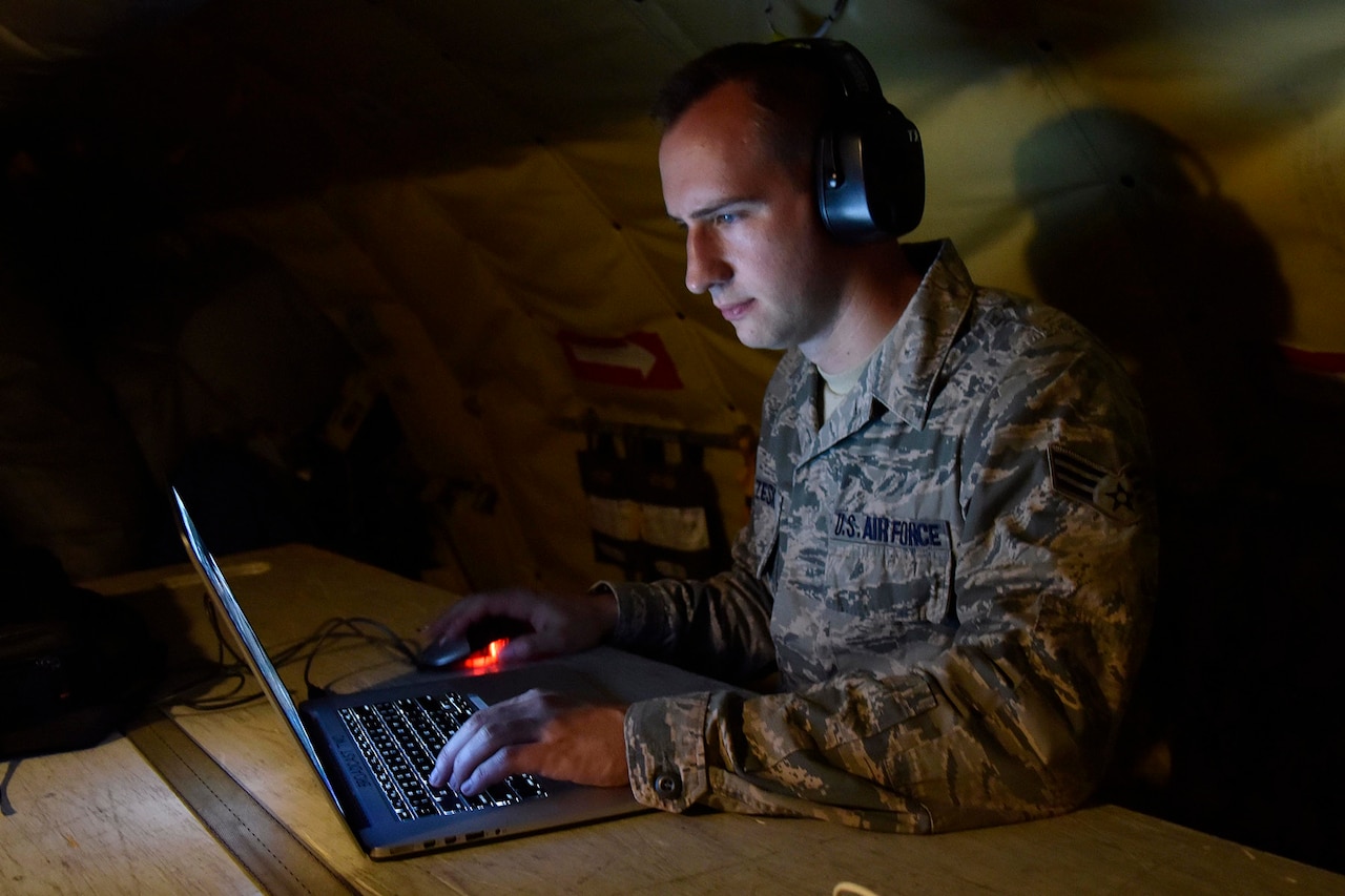 An airman clicks a mouse while looking at a laptop.