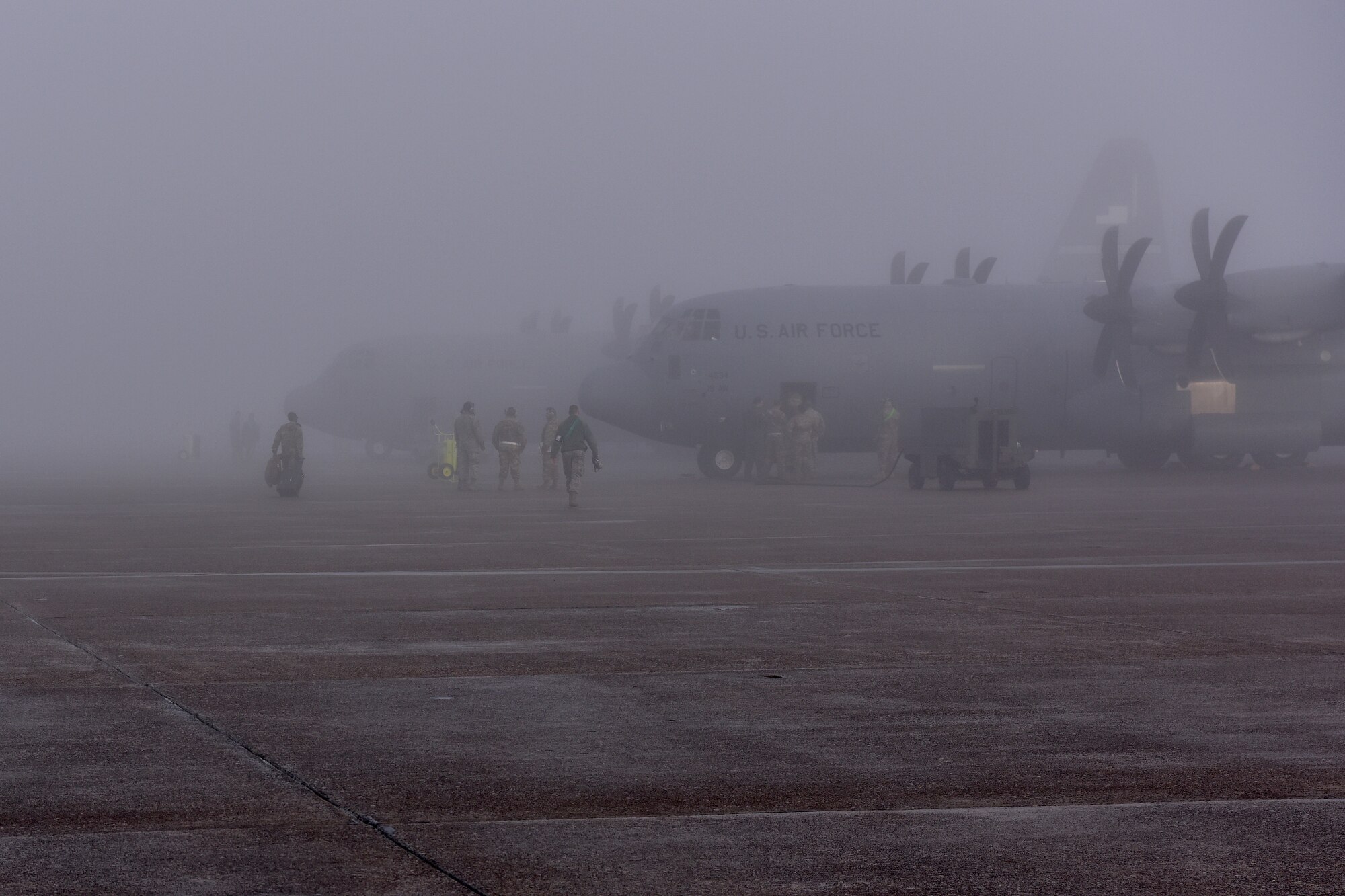 People walk in foggy area beside C-130Js on right of screen.