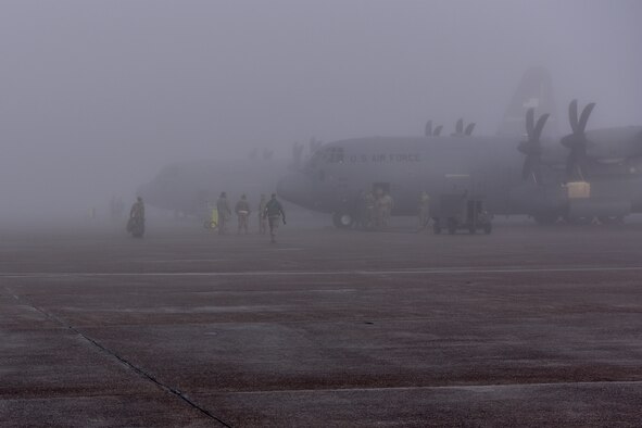 People walk in foggy area beside C-130Js on right of screen.