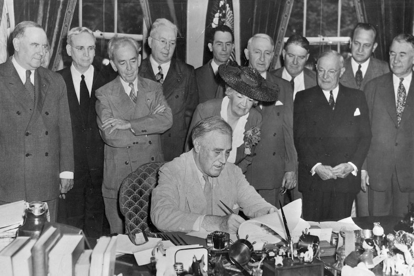 President Franklin D. Roosevelt signs the GI Bill at a table surrounded by people.