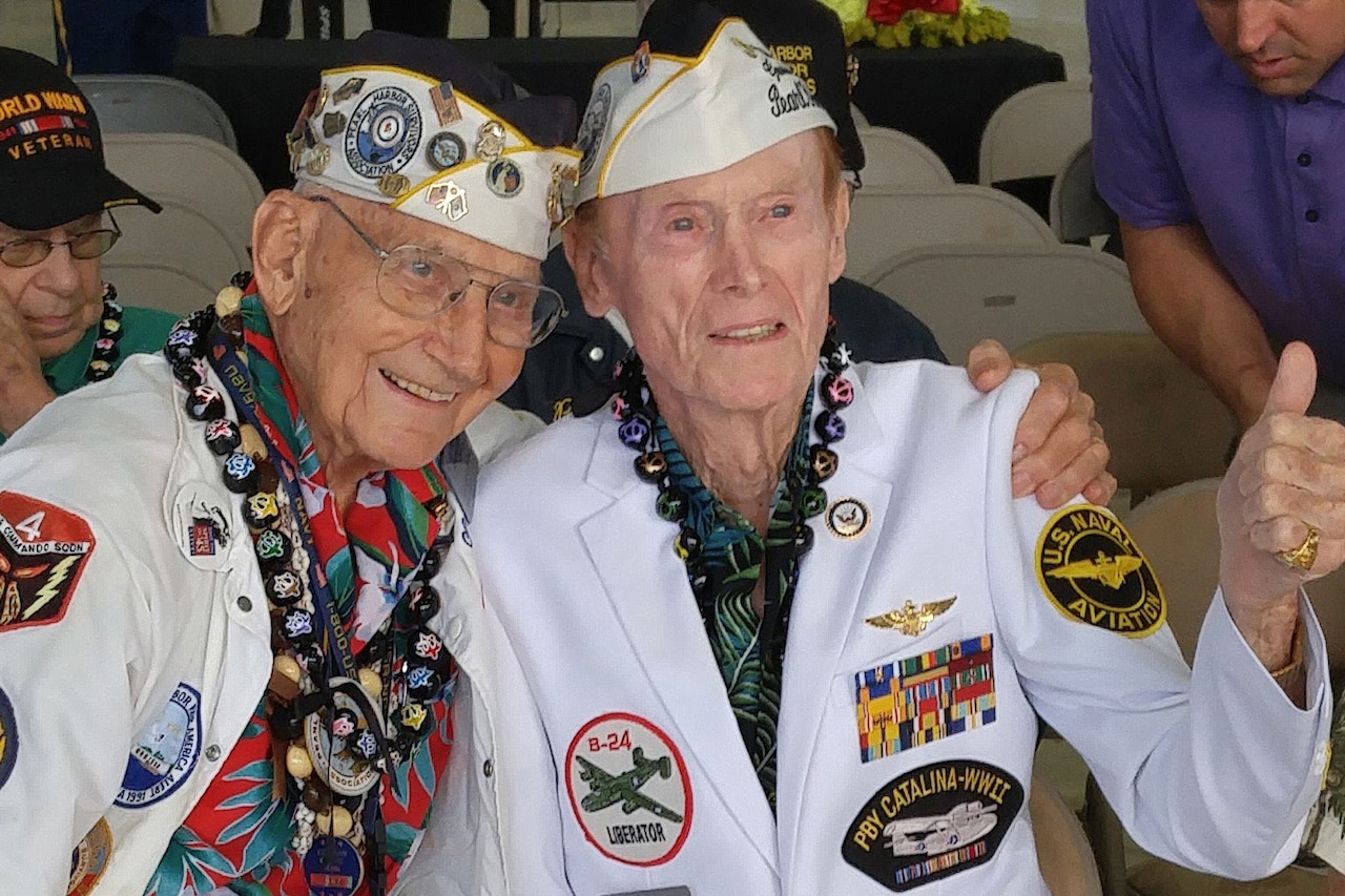 Two Pearl Harbor survivors hug and give a thumbs-up to the camera.