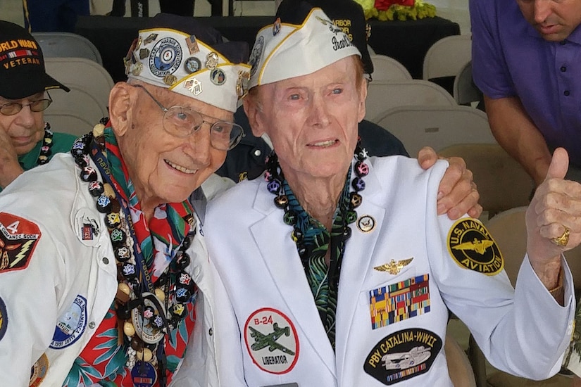 Two Pearl Harbor survivors hug and give a thumbs-up to the camera.