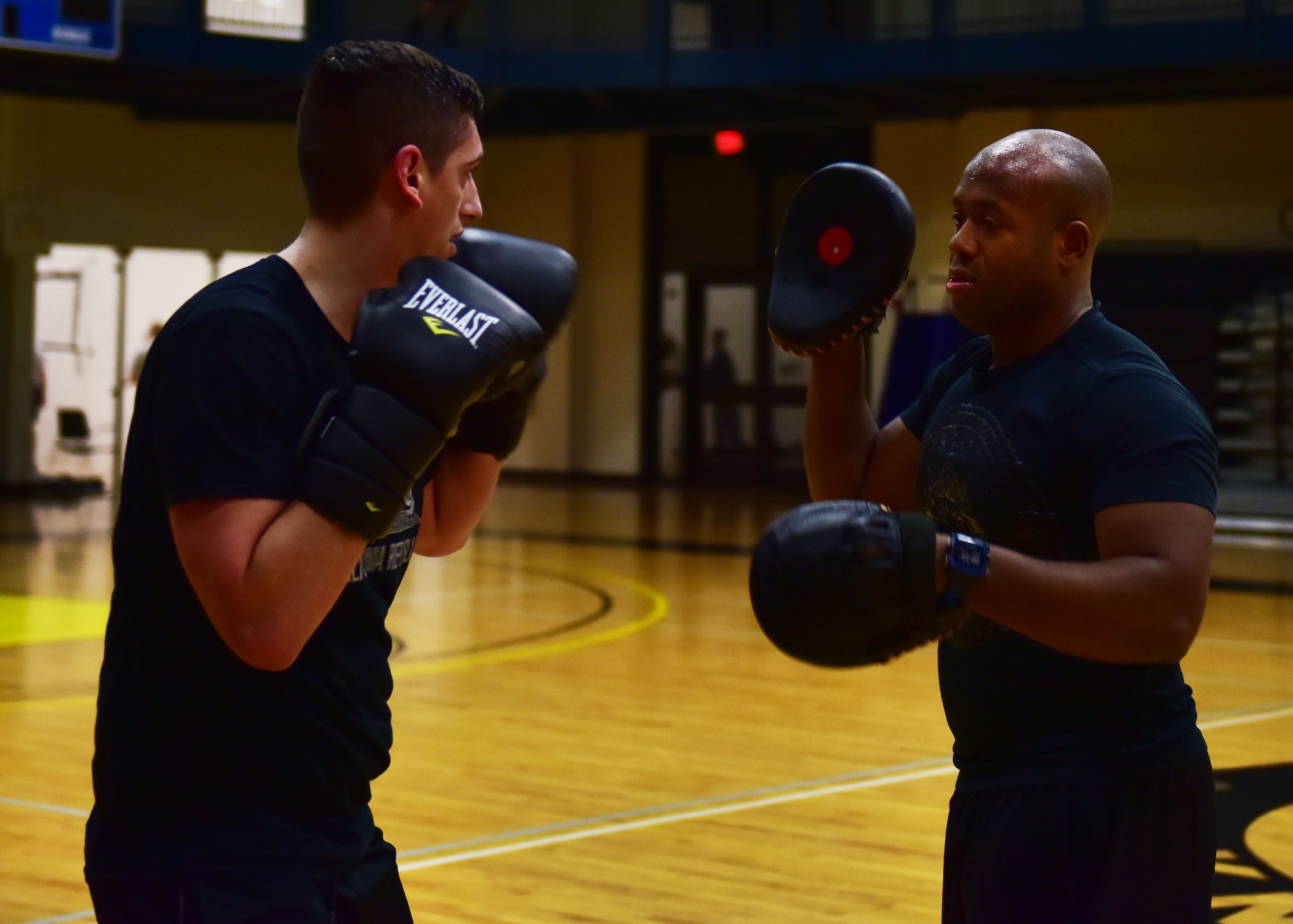 Two men wear boxing equipment practice boxing.