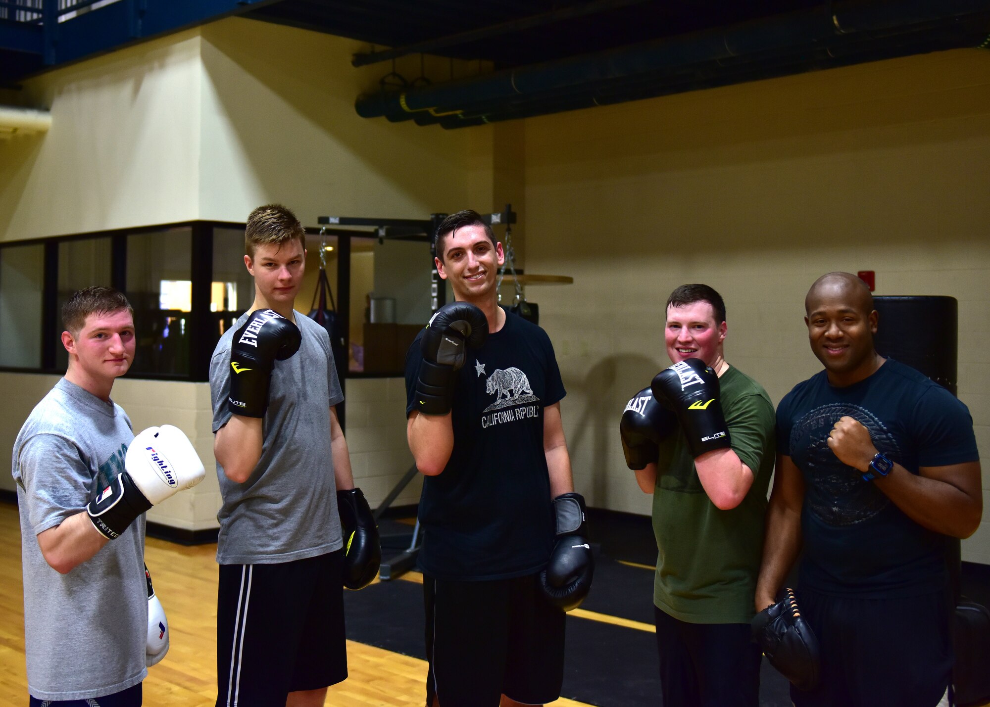 Five men in different workout clothes hold up their boxing gloves and smile at the camera.