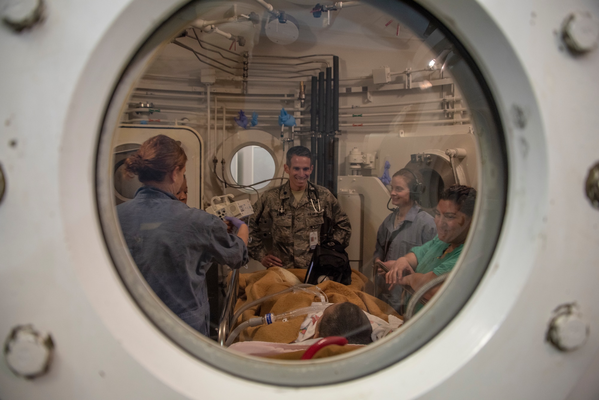 Lt. Col. (Dr.) Jason Kelly (center), 60th Aerospace Medicine Squadron, speaks to Jeremiah Harutyunyan, 11, a cancer patient receiving hyperbaric oxygen therapy treatment, Dec. 8, 2019, at David Grant USAF Medical Center, Travis Air Force Base, California. The hyperbaric oxygen treatment chamber uses state-of-the-art technology to aid patients who are in need of therapy for a multitude of diagnosed illnesses. HBOT provides the application of 100 percent oxygen, proven to increase blood flow and promote cell growth and new blood vessel formation. (U.S. Air Force Photo by Heide Couch)