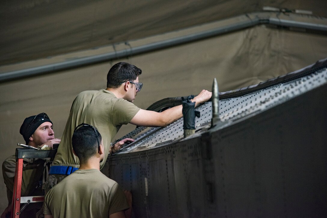 Three airmen work on a large aircraft component.