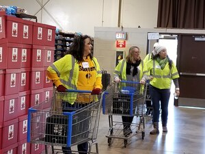 Three women in yellow push carts around warehouse