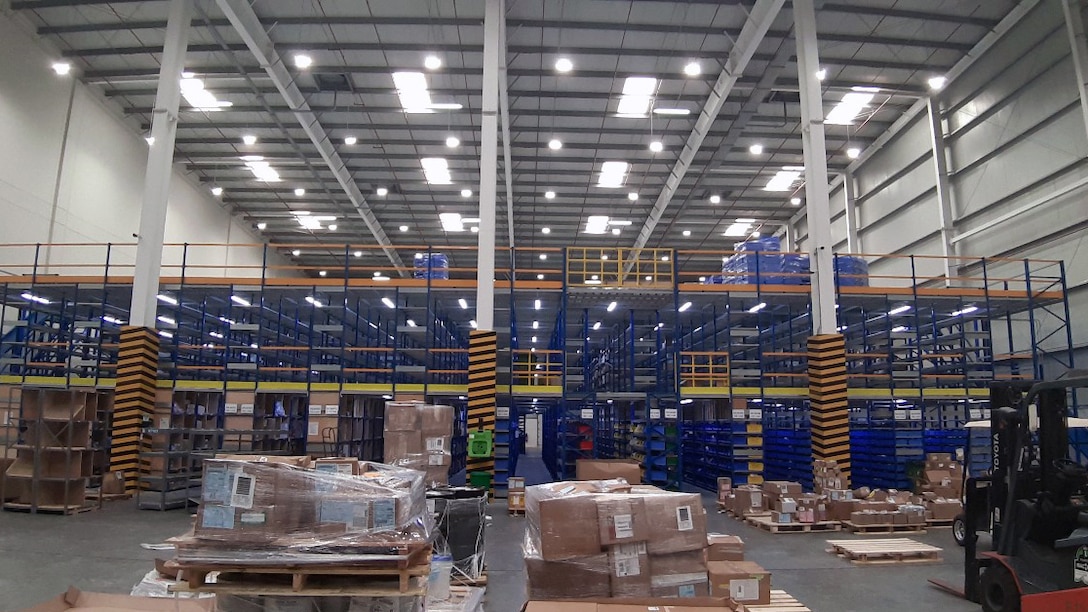 The interior of a bright warehouse with tall ceilings, vows of storage bin shelves and pallets of wrapped boxes in the foreground
