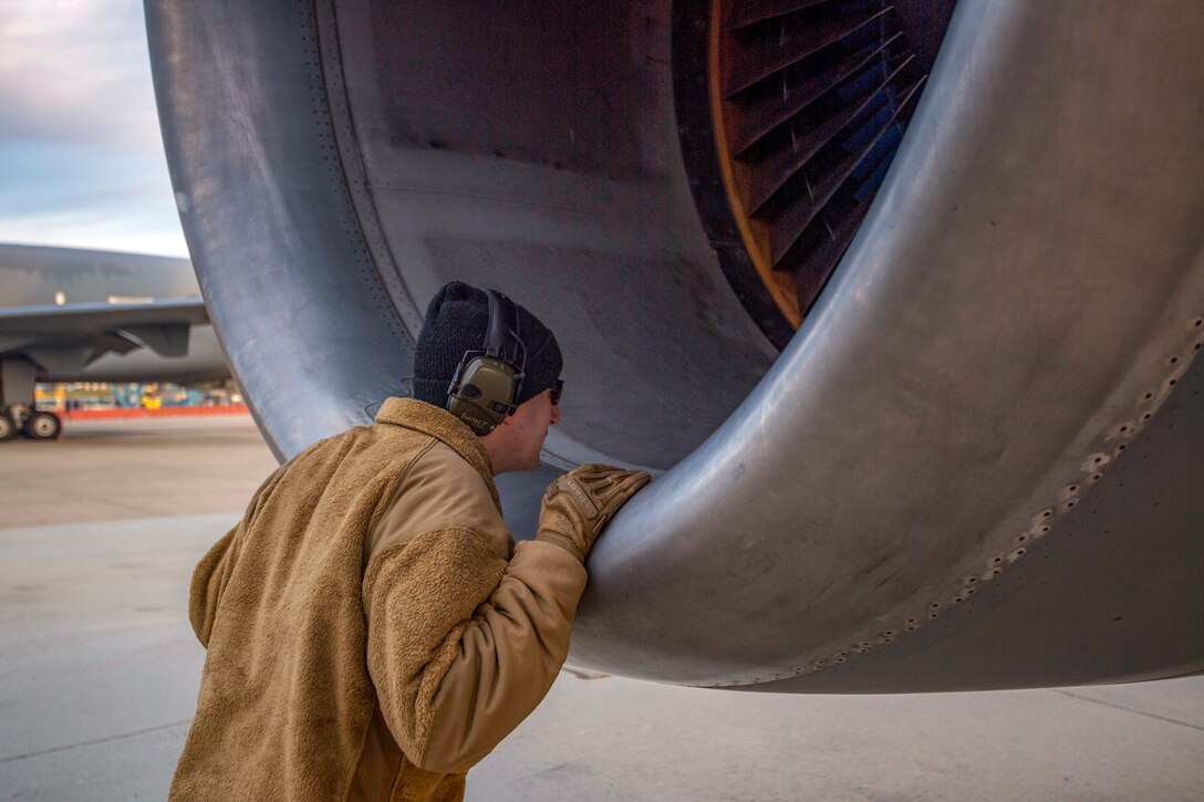 An airman sticks his head into an aircraft's engine.