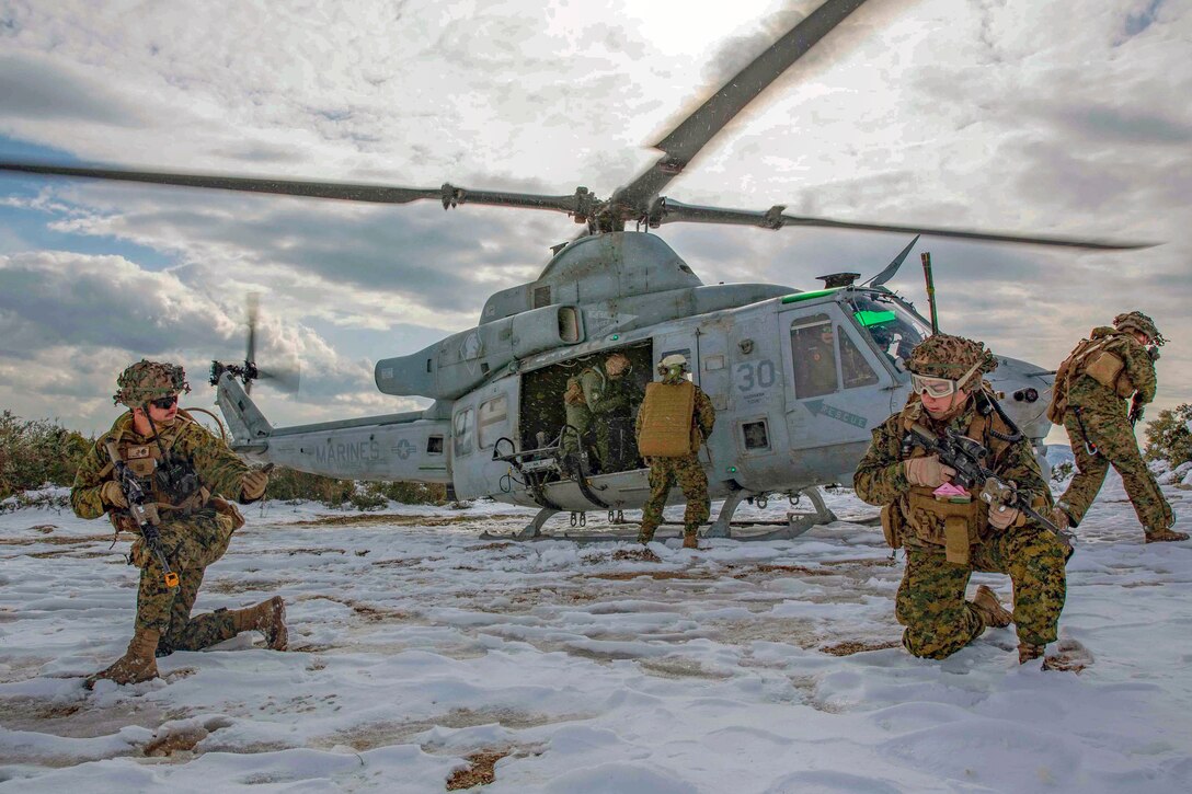 Marines exist from and crouch down around a helicopter in a snowy field.