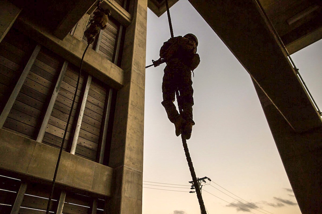 Marines descend down ropes hung from wooden platforms outside.