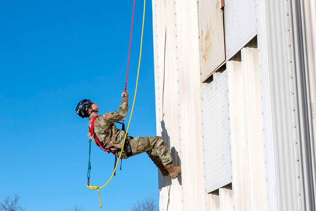 A soldier climbs a rope wall.