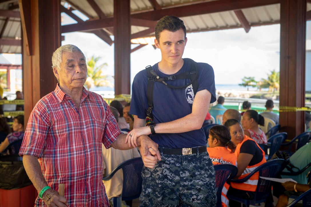 A U.S. service member holds an elderly man’s arm while helping him walk to get treatment at a medical clinic.