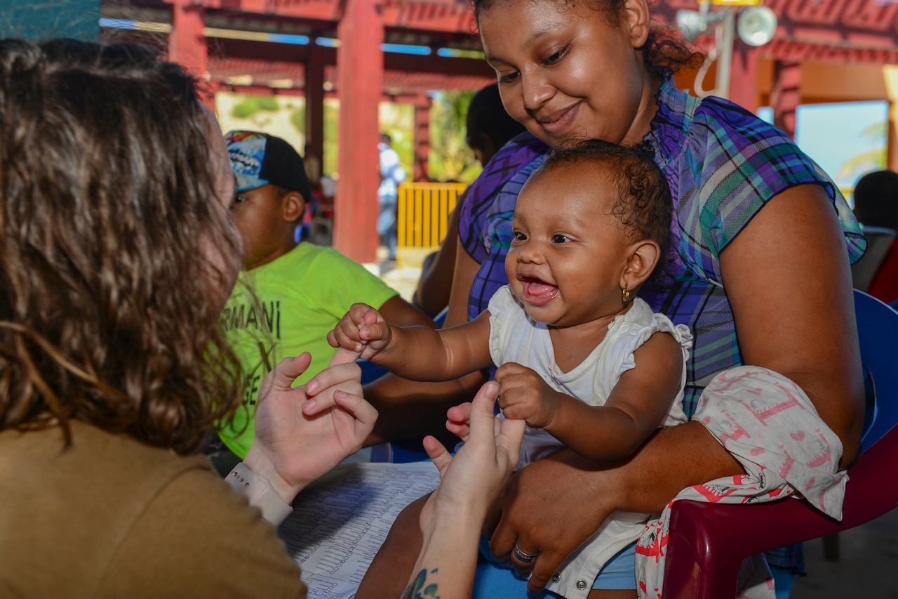 A U.S. service member plays with a toddler being held by her mom.