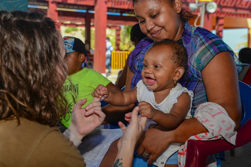 A U.S. service member plays with a toddler being held by her mom.