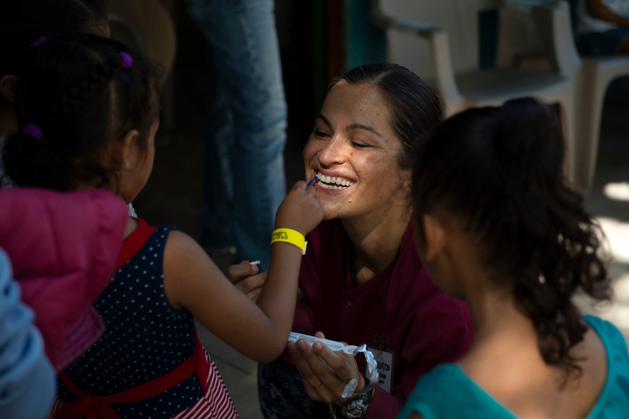 A U.S. service member teaches a girl to brush her teeth.