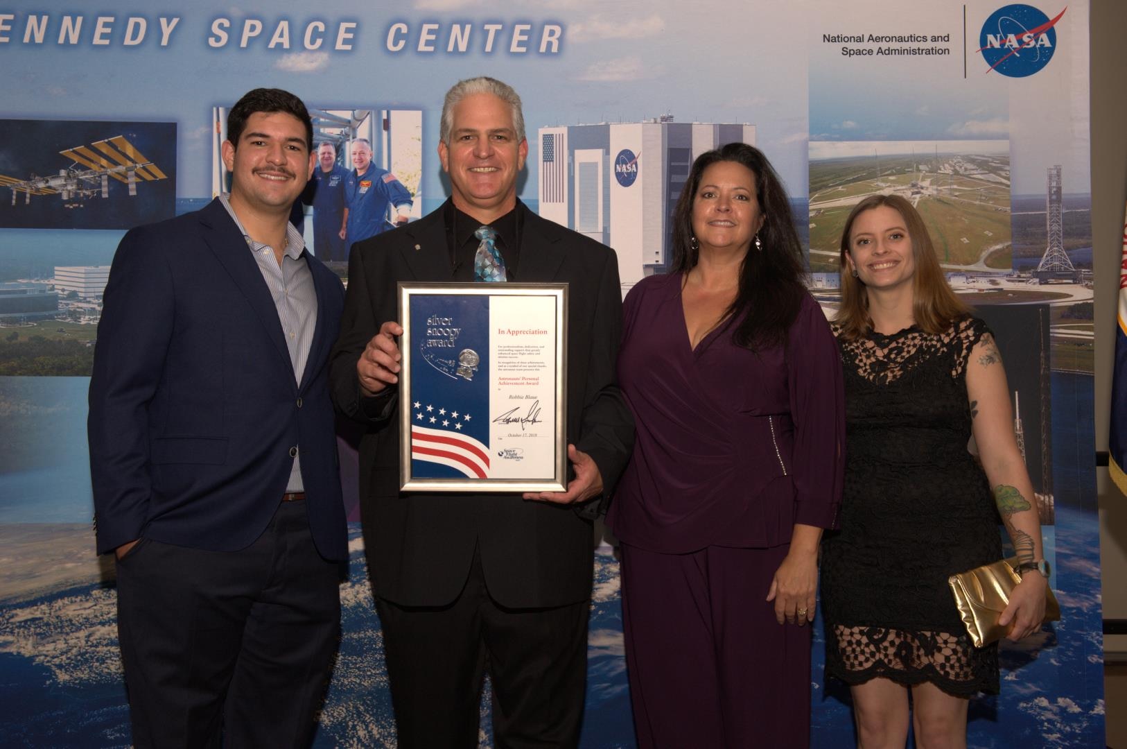 A man with his award posing with his wife and two children