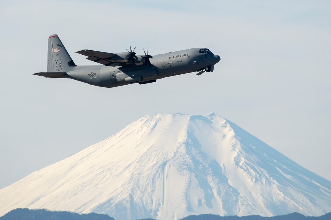 A plane ascends in the sky with a mountain in the background.