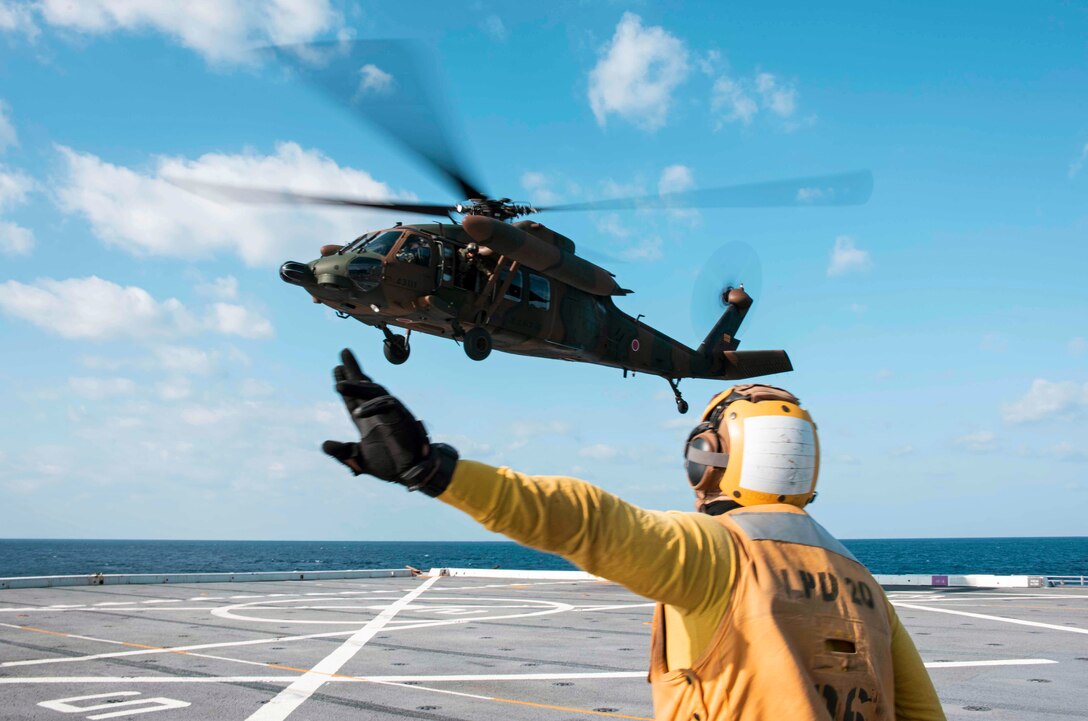 A sailor points signals to a Black Hawk helo on the deck of a ship.