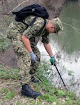 Seaman Ryan Shorter, who was training to become a medical corpsman at the Medical Education and Training Campus at Joint Base San Antonio-Fort Sam Houston, reaches for a piece of trash along Salado Creek during the annual Basura Bash Feb. 17, 2018.