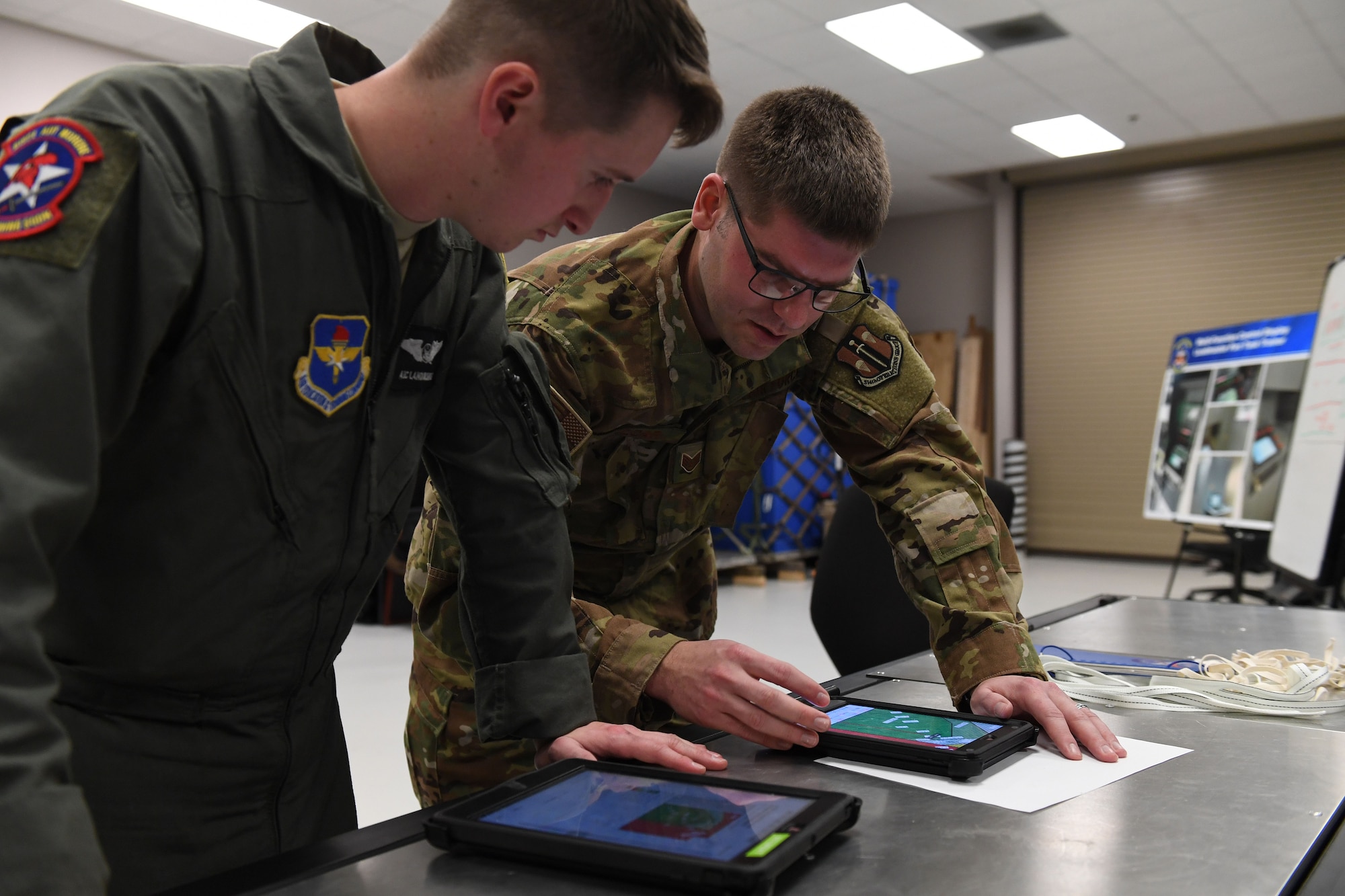 Two men are bent over a table, while looking at a tablet.