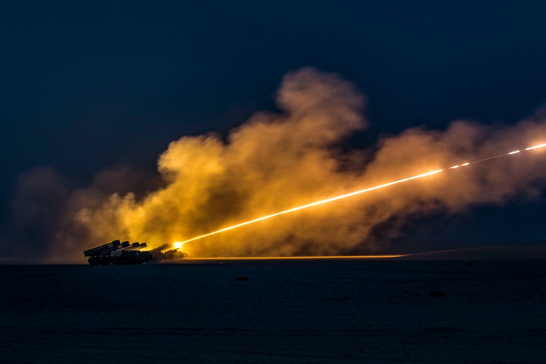 Soldiers fire mobile artillery rockets in the desert.