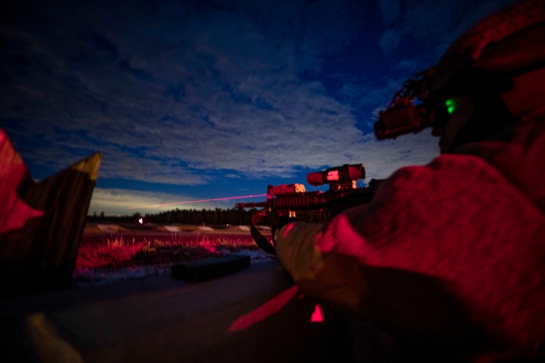 A soldier, illuminated in pinkish light, fires a weapon into a vivid blue night sky.