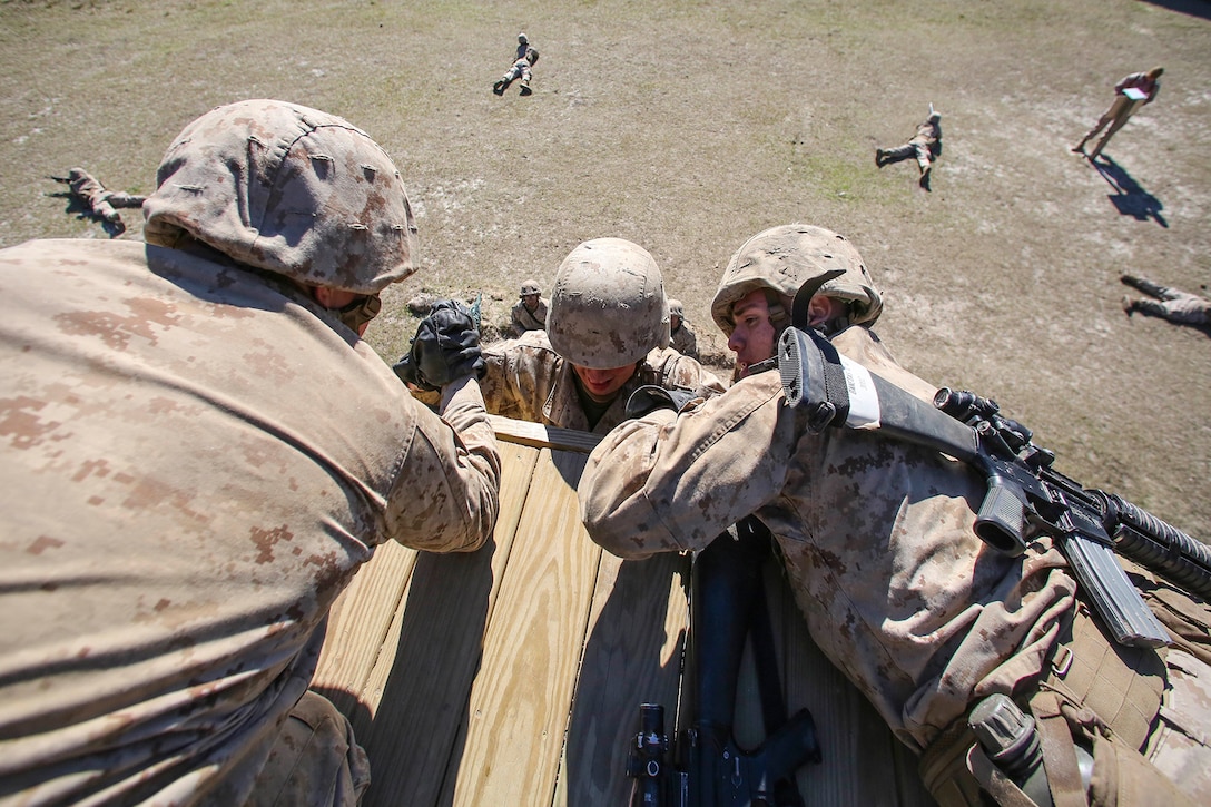 Marine Corps recruits help a fellow recruit over an obstacle.