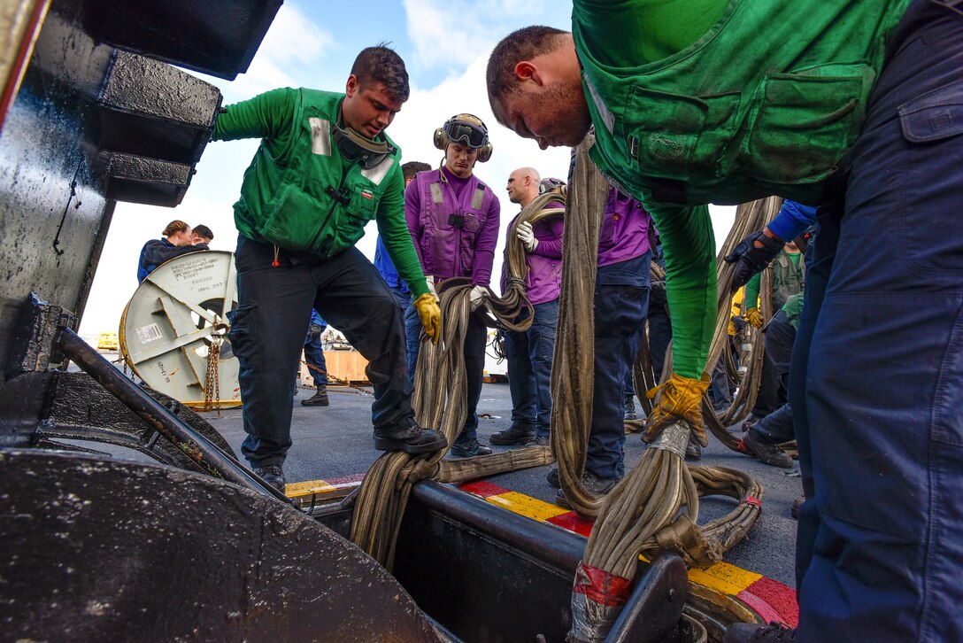 Sailors place lines into a stowage space.