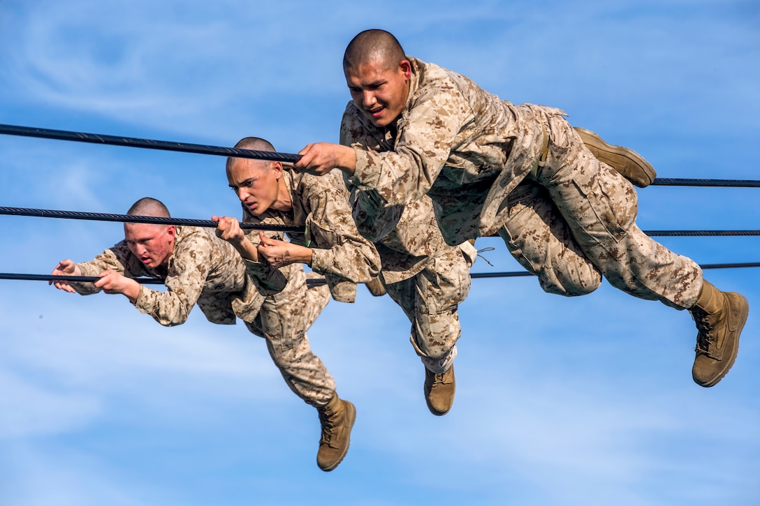 Three Marines slide across ropes as part of an obstacle.