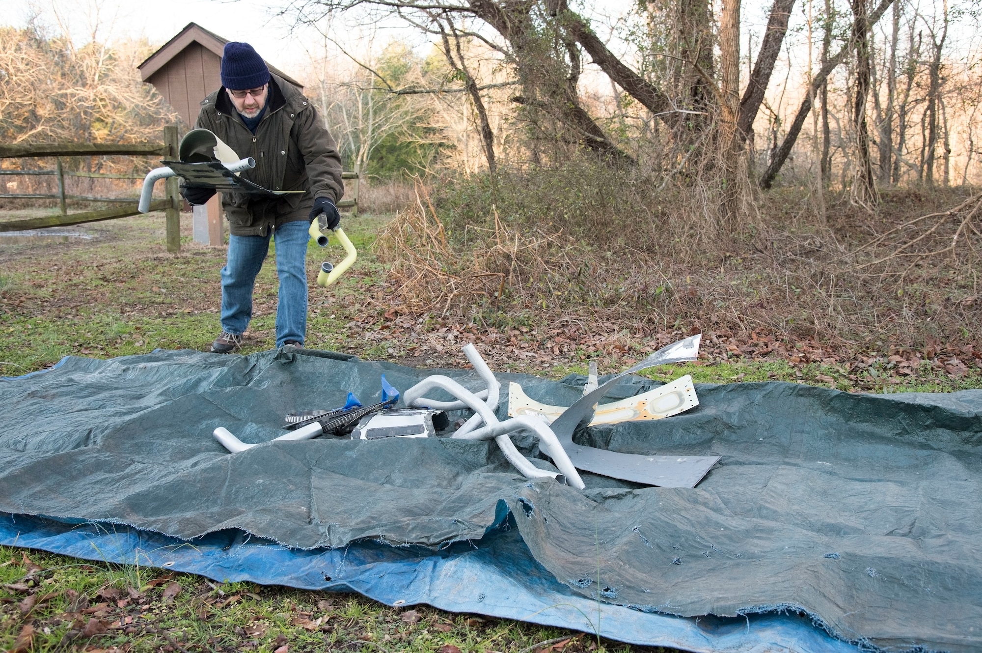 Simon Lowe, 436th Civil Engineer Squadron engineering technician, places condemned aircraft parts on a tarp prior to an aircraft mishap survey exercise Dec. 18, 2018, near Killens Pond State Park, Kent County, Del. Lowe placed about 45 miscellaneous aircraft and aircrew items for 436th CES engineering assistants to practice plotting and documenting the items using GPS equipment and a digital camera. (U.S. Air Force photo by Roland Balik)