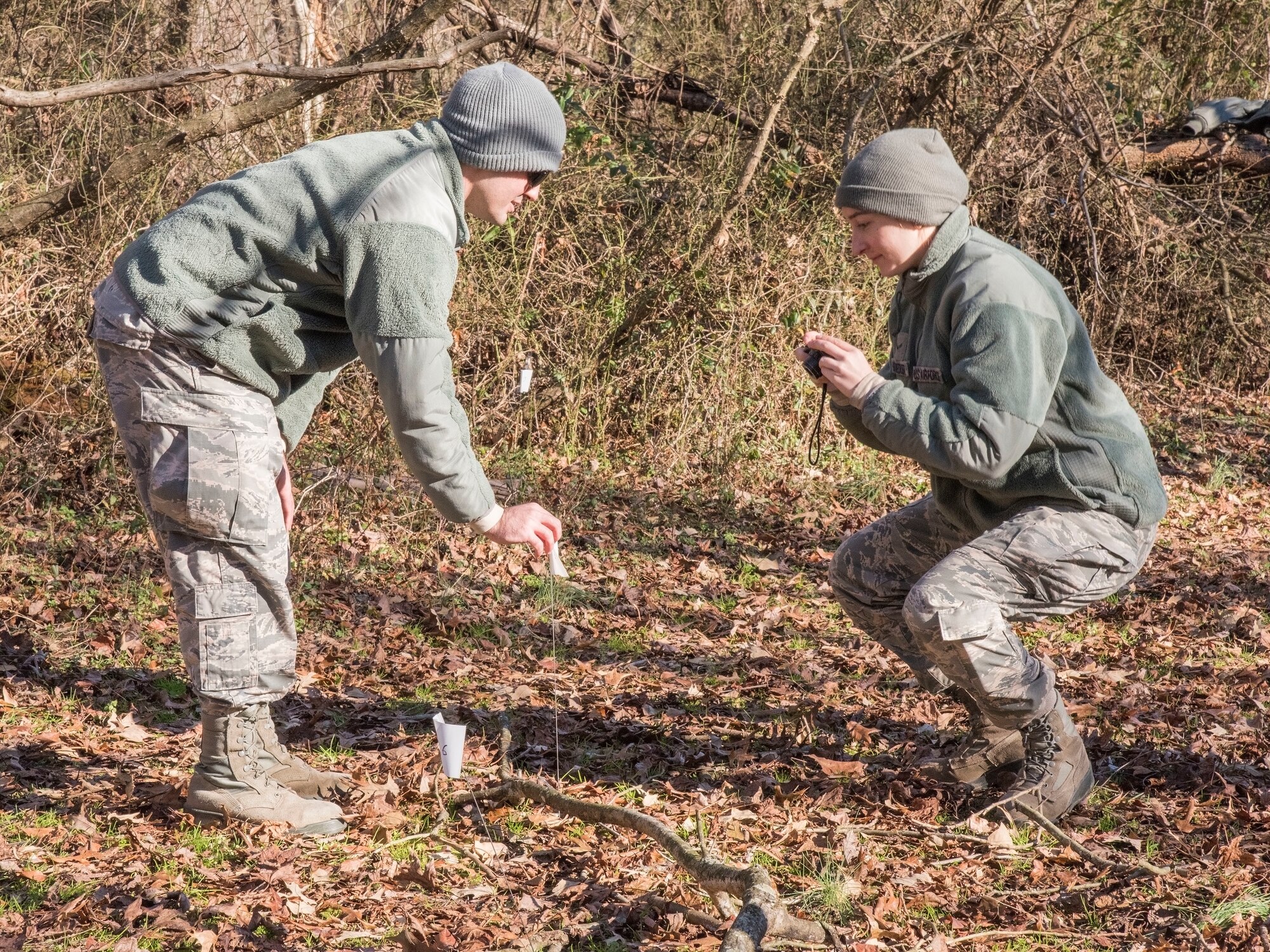 Airman 1st Class Taylor Hawk and Angela Schnedler, both 436th Civil Engineer Squadron engineering journeymen, documents a flagged item in a simulated debris field during an aircraft mishap survey exercise Dec. 18, 2018, near Killens Pond State Park, Kent County, Del. Documenting debris locations with a corresponding digital photograph aids investigation boards in determining the cause of an accident. (U.S. Air Force photo by Roland Balik)