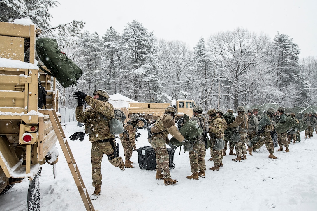 A group of soldiers stand in a line loading a truck in the snow.