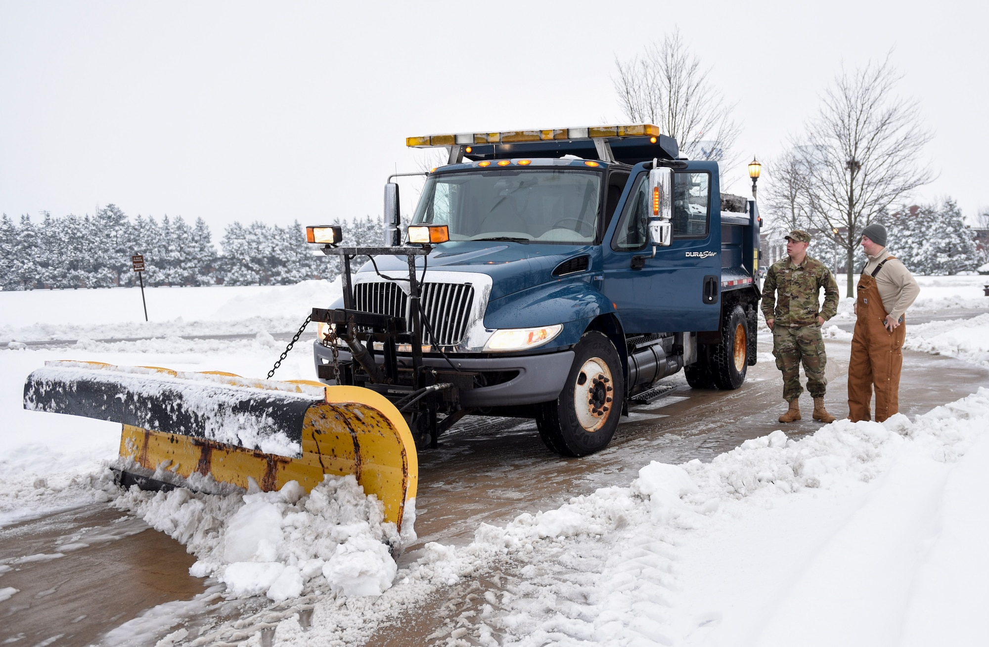 Senior Airman Caleb Lyons, 375th Civil Engineer Squadron water and fuels system maintenance, speaks with Staff Sgt. Justin Henke, 375th CES electrical systems journeyman about clearing the roads  Jan. 12, 2019, after heavy snowfall hit Scott Air Force Base, Illinois. The initial road clearing process takes about three hours but must be continued for as long as the snow is falling to ensure people stay safe.