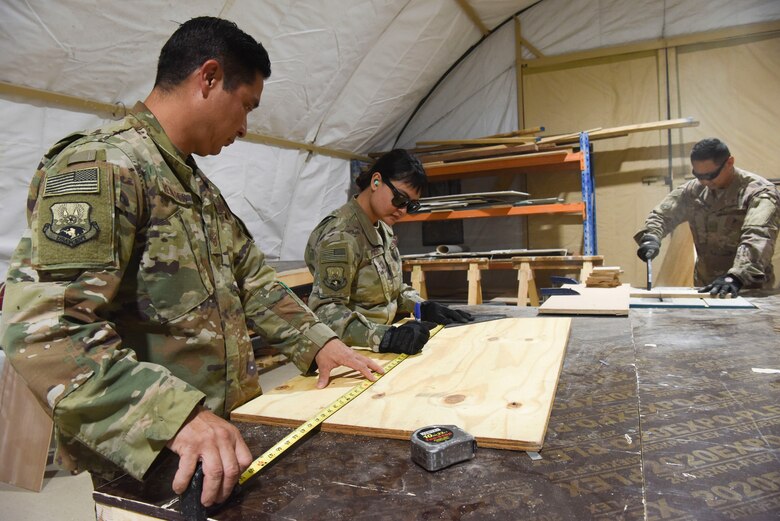 624th Civil Engineer Squadron Reservists Tech. Sgt. Victor Reinares, 380th Expeditionary Civil Engineer Squadron structures mid-shift shop lead, and Staff Sgt. Valeesa Conley, 380th ECES structures technician, measures wood so Staff Sgt. Ryan Ang, 380th ECES structures technician, cuts it for a work order, Jan. 9, 2019 at Al Dhafra Air Base, United Arab Emirates.