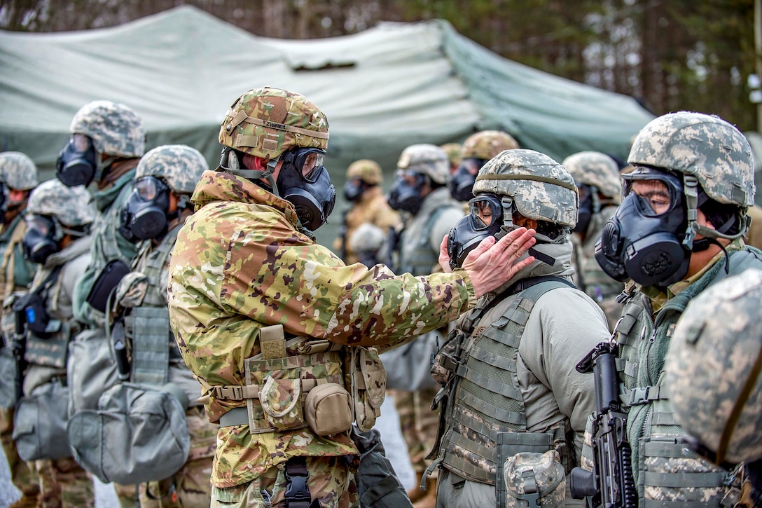 A soldier holds another soldier face in a mask in his hands, examining it closely.