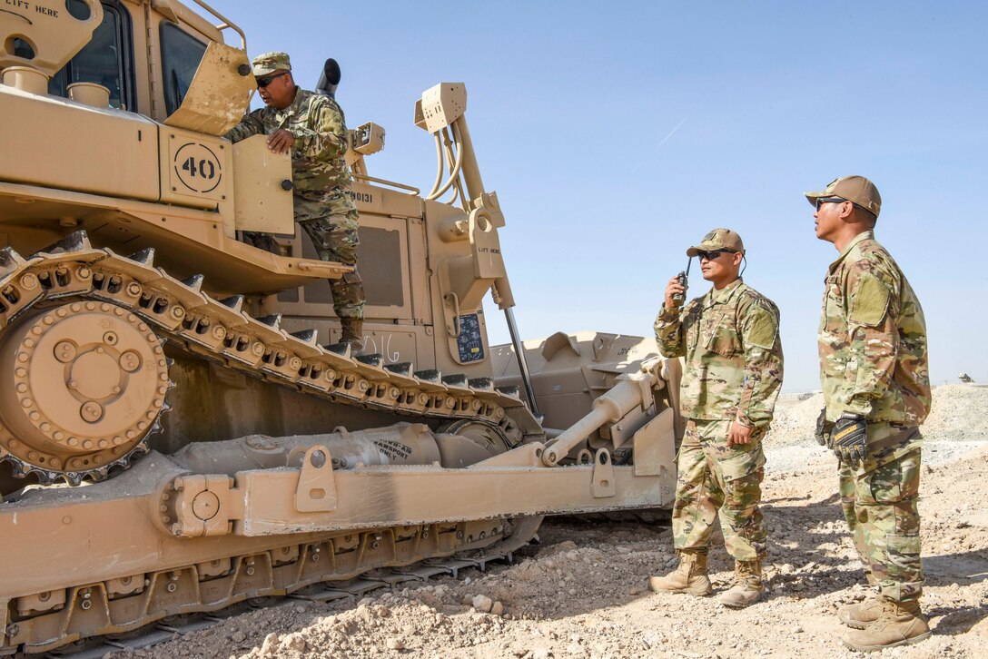 Airmen inspect a bulldozer parked on desert-type terrain.