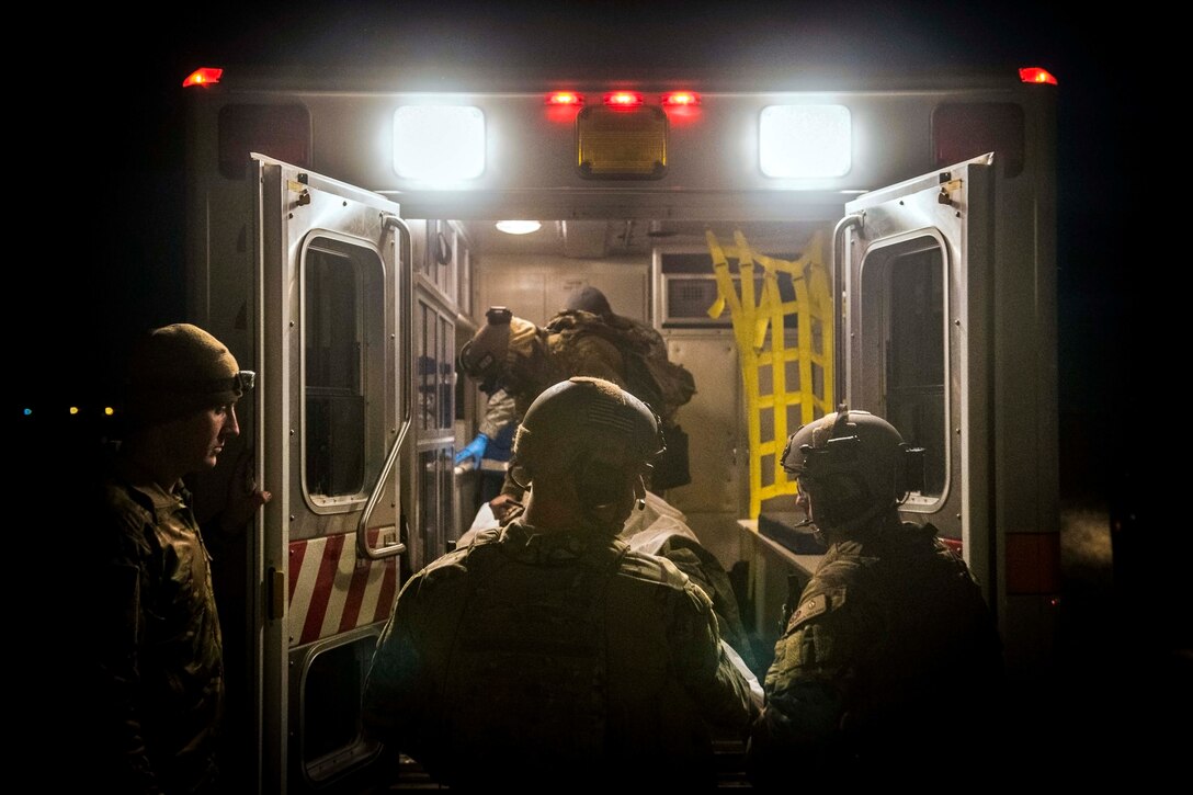 Airmen move people into an ambulance at night.