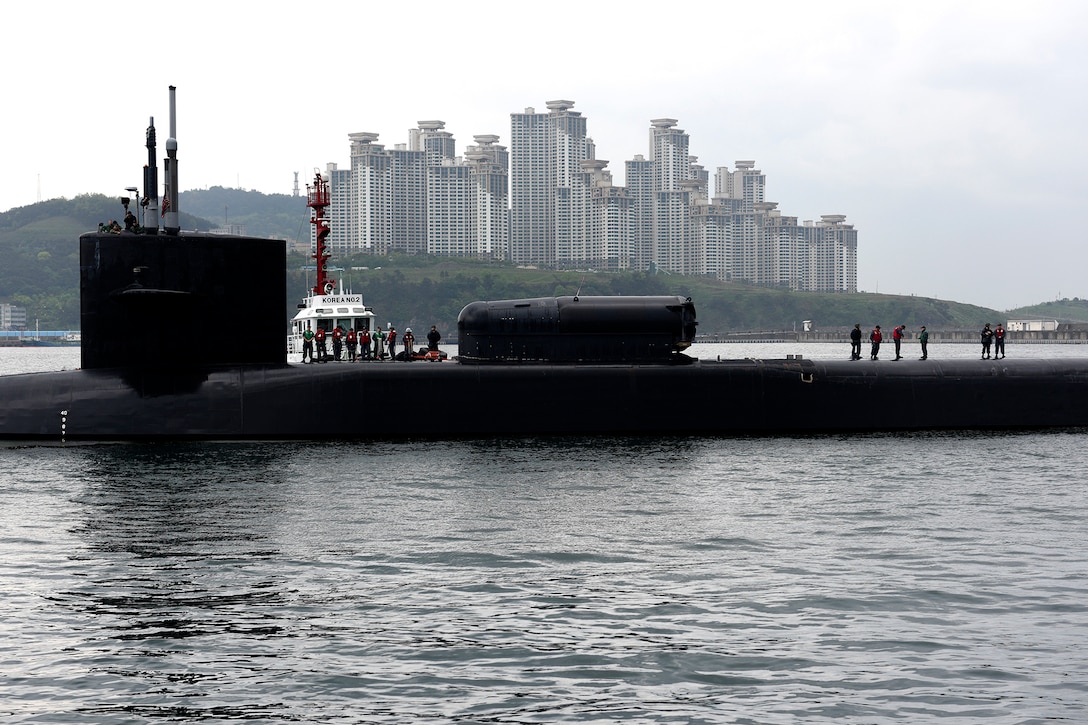 Several sailors stand on top of a submarine floating near shore.