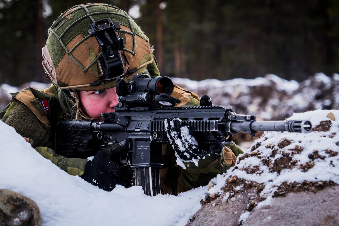 A Norwegian soldier aims a carbine in snowy conditions.