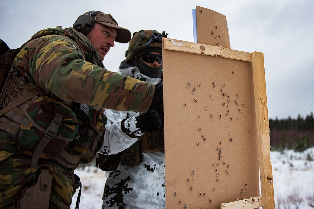 A Belgian and a German soldier examine a rifle target.