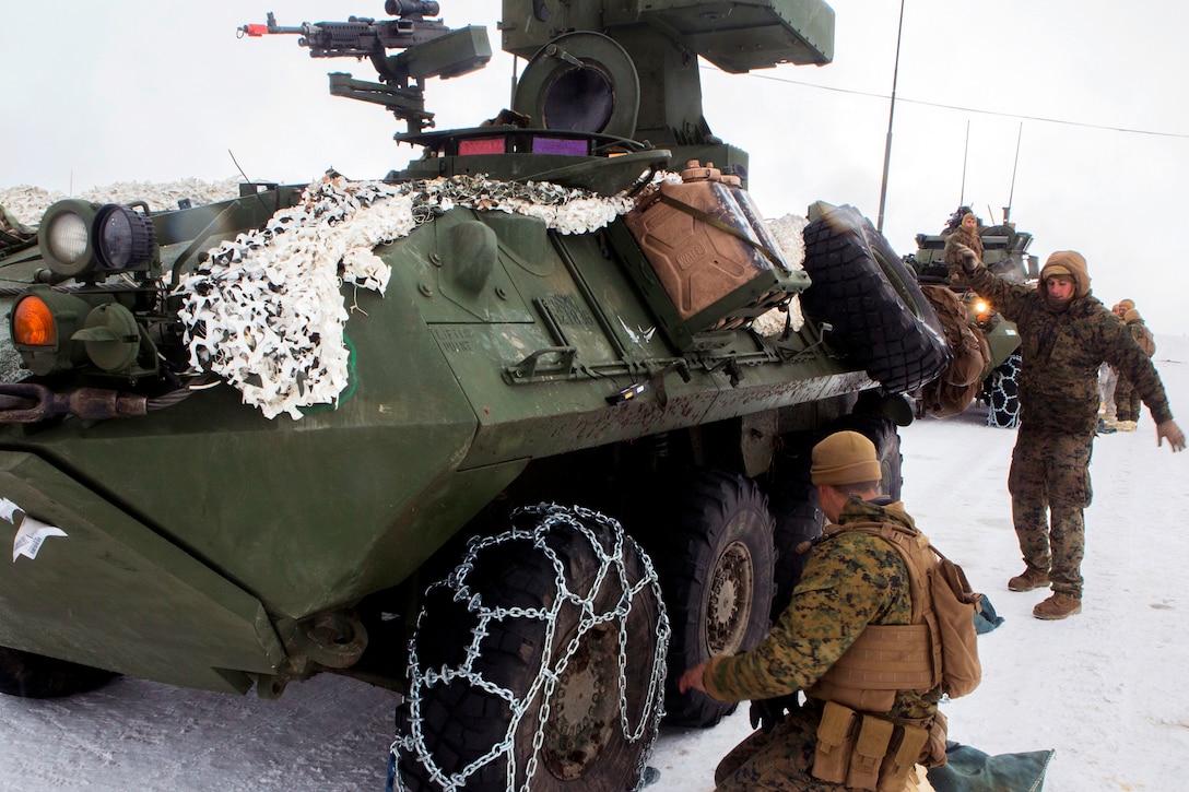 Marines and sailors install snow chains on the tires of a light armored vehicle.