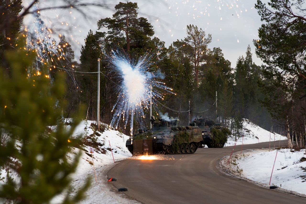 A tank round simulator explodes near two infantry combat vehicles.