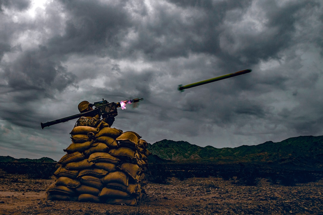 A Marine fires a missile from behind sandbag cover.