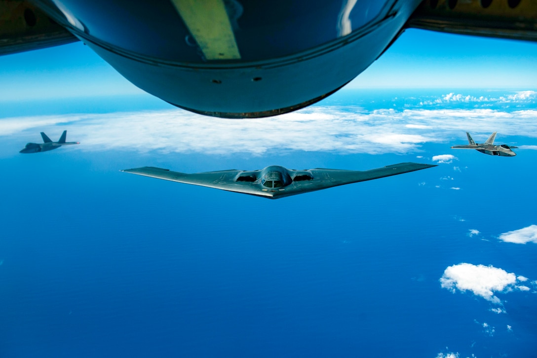 A B-2 bomber flies over the ocean with two other planes at its side.