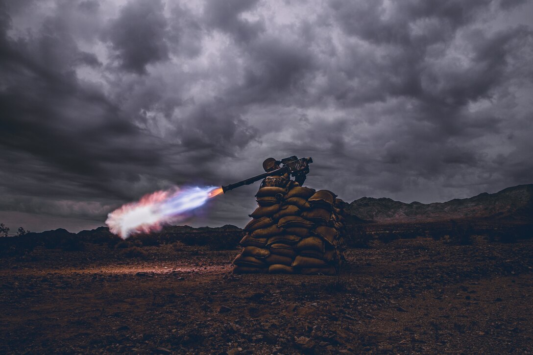 A Marine fires a missile while sitting on top of sand bags.