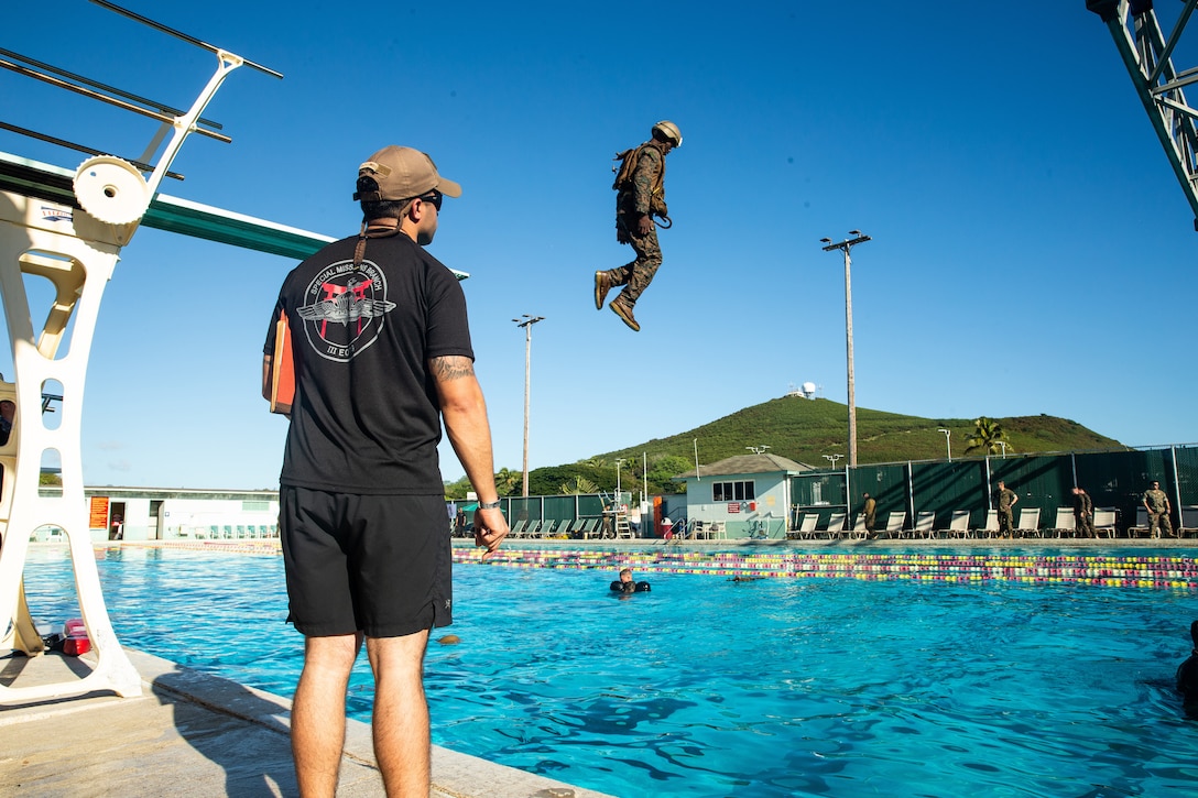 A man watches a Marine dive into a swimming pool.