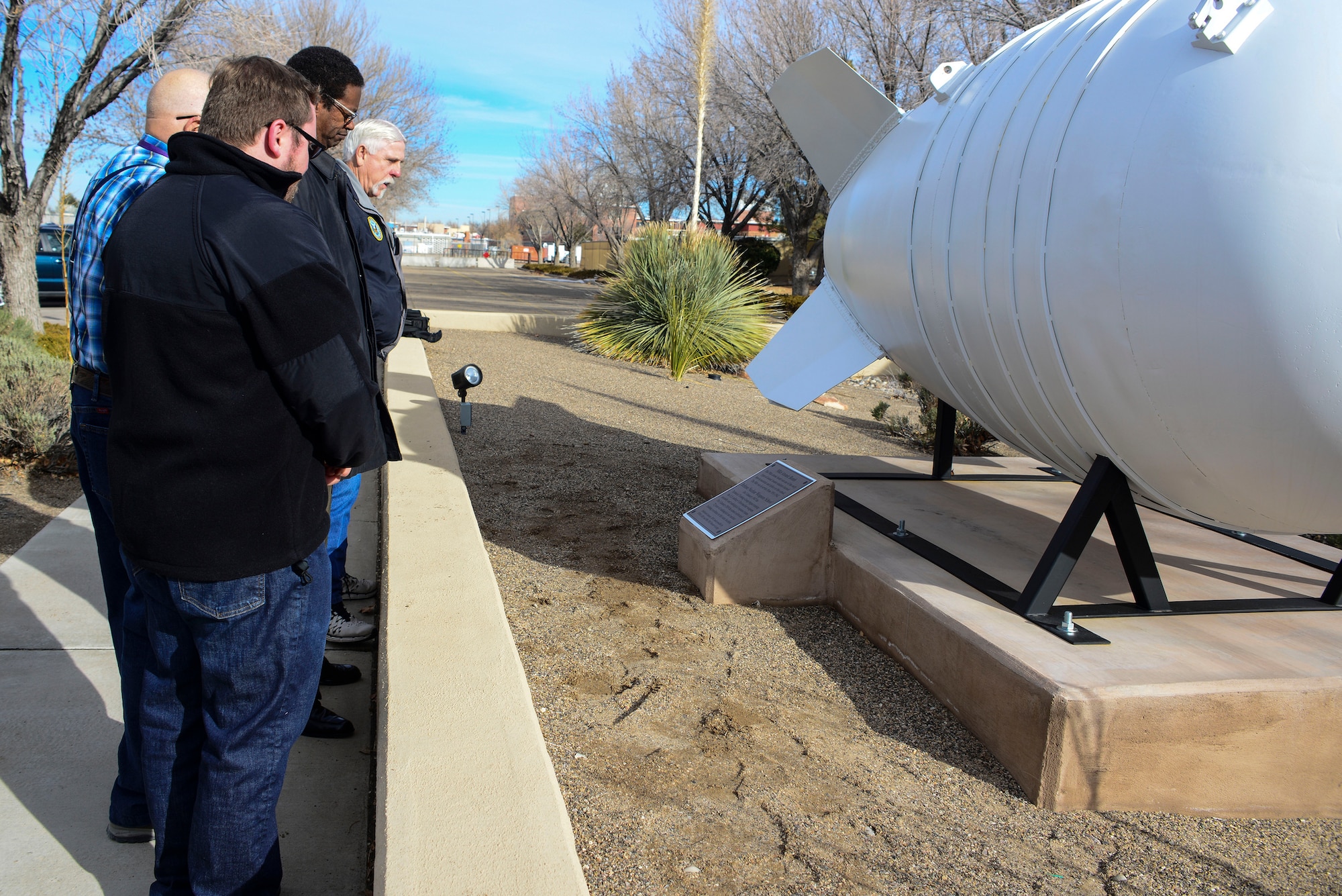 Members of the dedication ceremony read the plaque placed in front of an iconic Mk6 Atomic Bomb replica training device that was unveiled in front of the Defense Nuclear Weapons School at Kirtland Air Force Base, N.M., Jan. 10. The DNWS mission is to provide Nuclear Enterprise and radiological education and training in support of Joint service, interagency organizations, and foreign partners worldwide. (U.S. Air Force photo by Staff Sgt. Kimberly Nagle)
