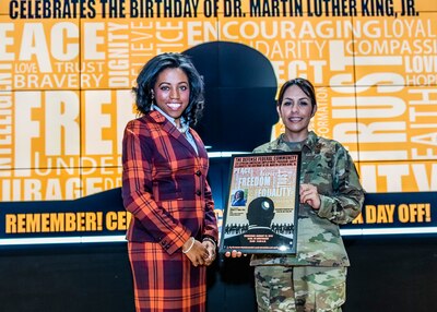 Keynote speaker and Chief of Staff stands on stage holding a framed poster